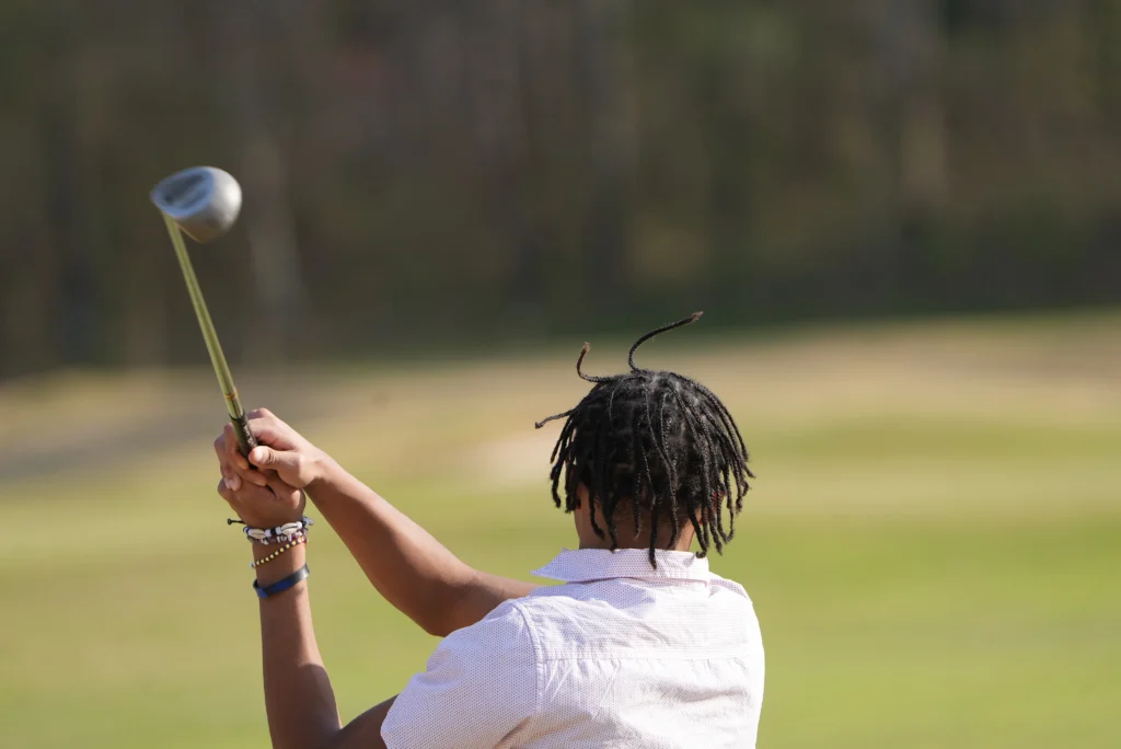 A man with dreadlocks swinging a golf club photo